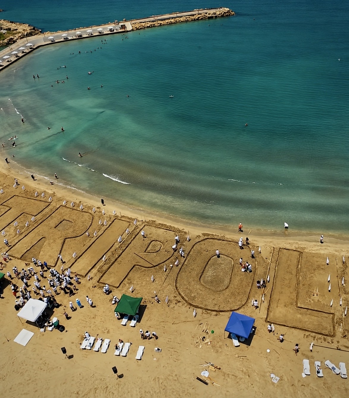 Aerial view of a beach event and large sand sculpture beside the sea