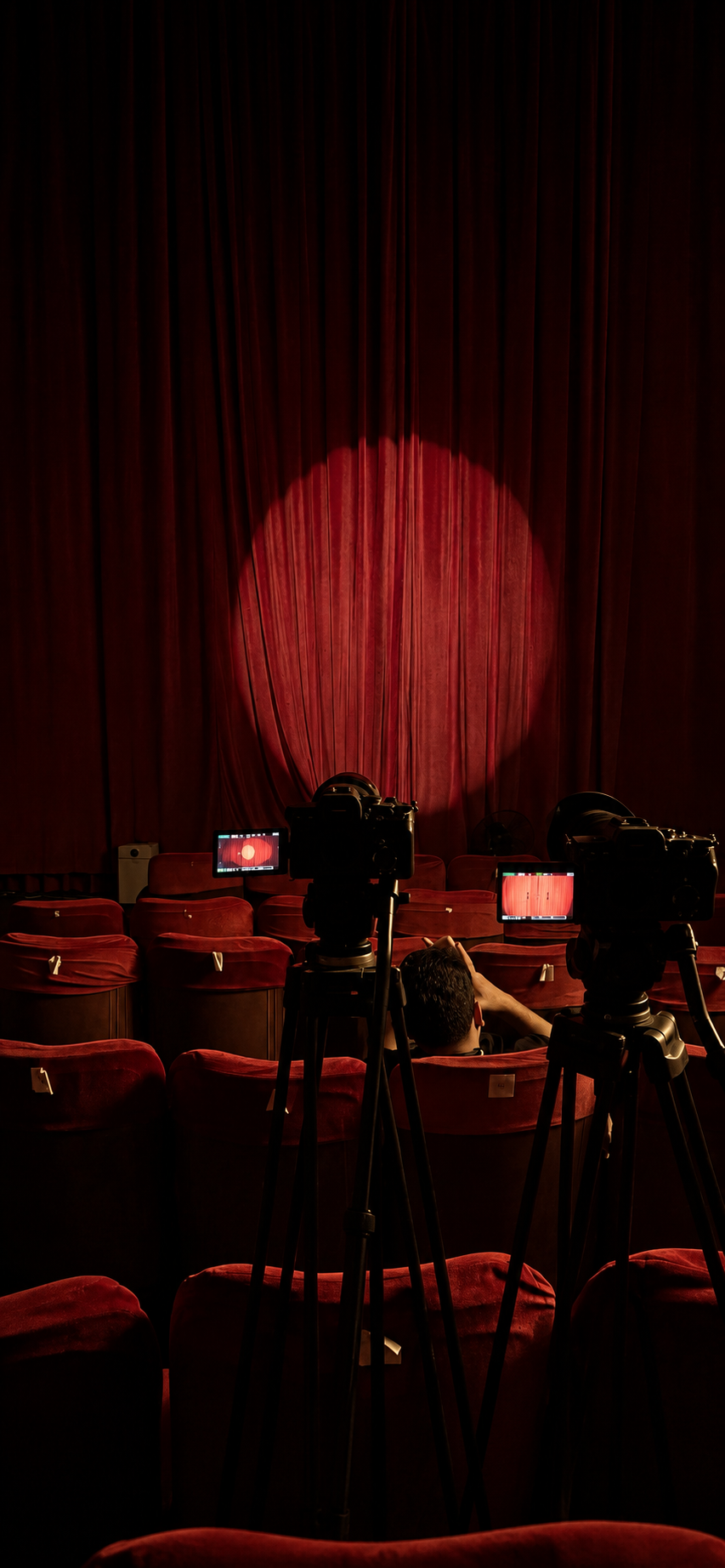 Cameras filming a theater stage under a red spotlight